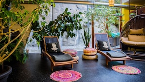 Un espace de détente intérieur, chaleureux, avec des fauteuils confortables, une grande plante en pot et un mur agrémenté d’une cascade.