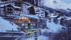 Un hôtel enneigé, doté de plusieurs étages, de balcons et surplombant un paysage montagneux.