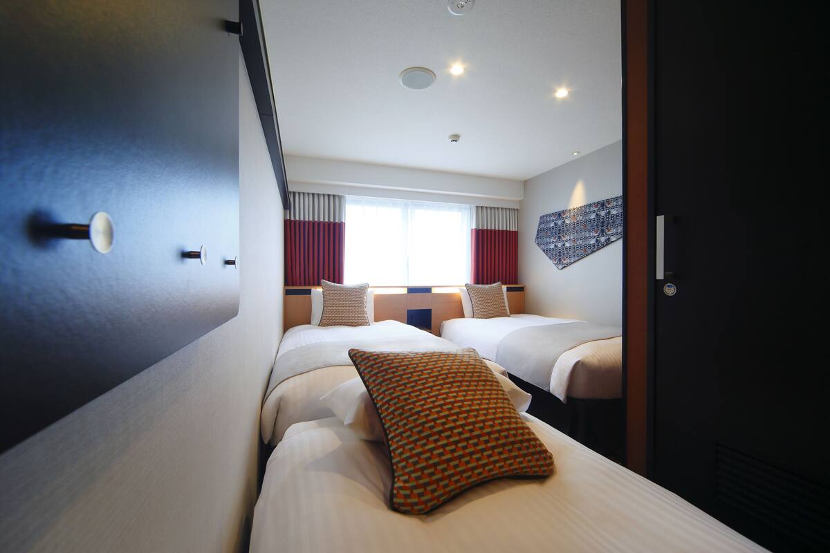Habitación de hotel con dos camas, un ventanal con cortinas rojas y un adorno en la pared.