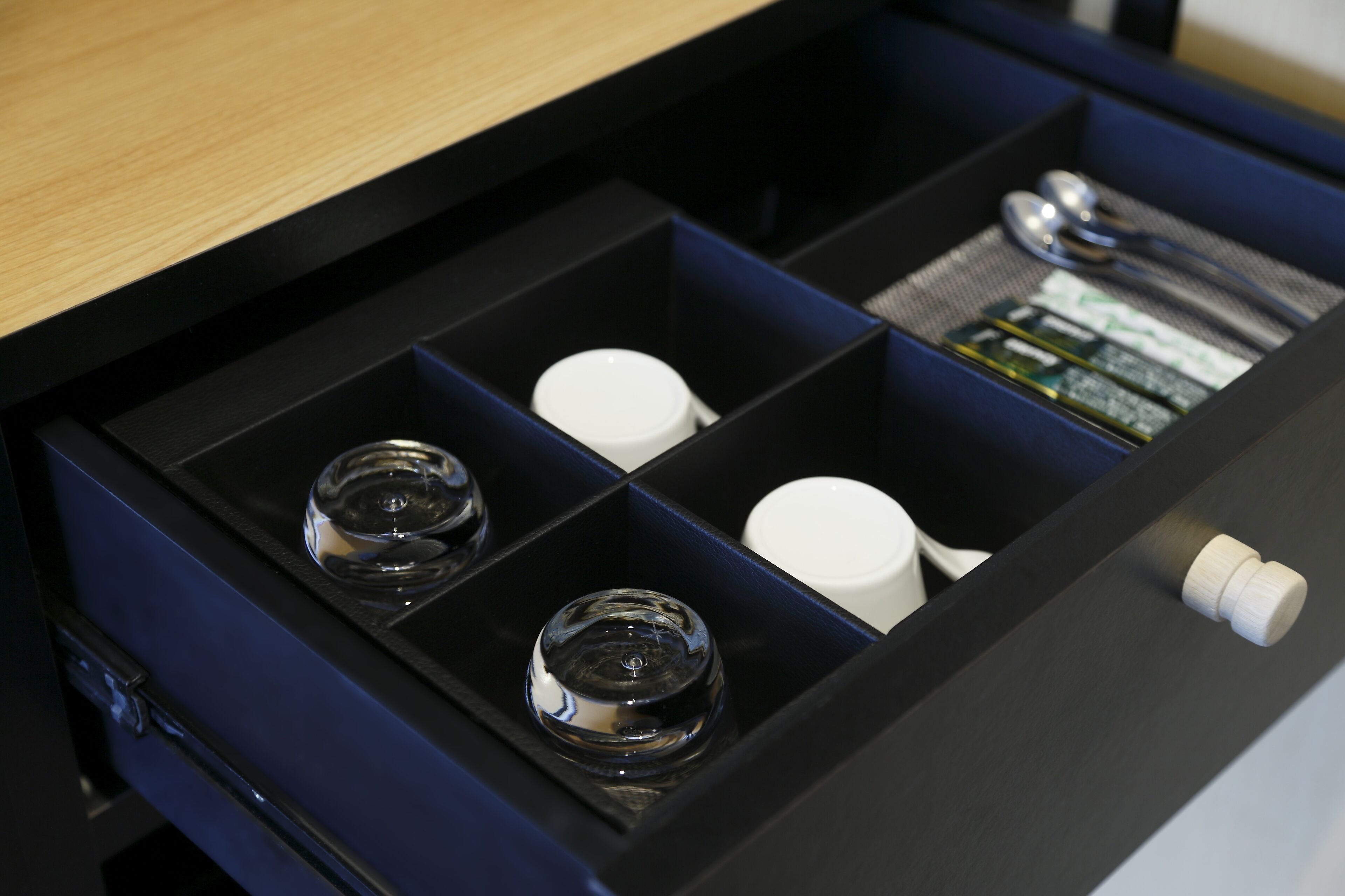 A drawer with compartments containing various items including bottles and a spoon.
