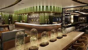 Zona de bar moderna con un mostrador curvo, paredes verdes y varias cúpulas de vidrio iluminadas sobre la barra.
