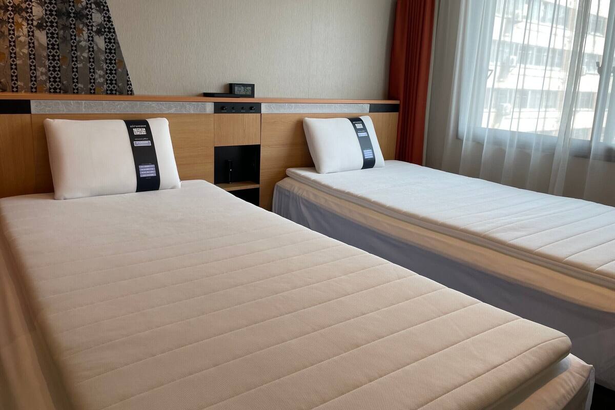 Una habitación de hotel con dos camas, un cabecero, una mesita pequeña y un reloj.