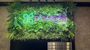 Un letrero de neón del 'D'Garden Hotel' con un exuberante muro verde de fondo.