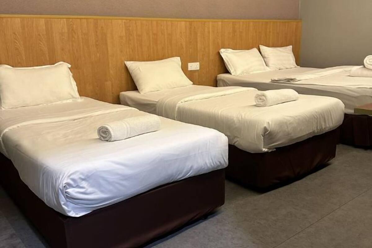 A hotel room with three beds, each with white linens and pillows, a wooden headboard, and a carpeted floor.