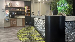 Una zona de recepción moderna con estación de café, un letrero que dice 'HOT DRINKS' y una pared verde con la palabra 'GARDEN'.