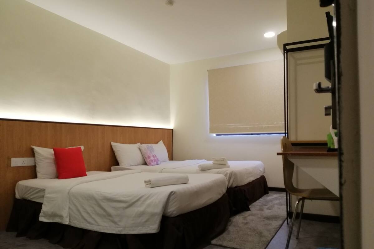 A hotel room with two beds, a wooden headboard, a small desk, and a window with a blind.