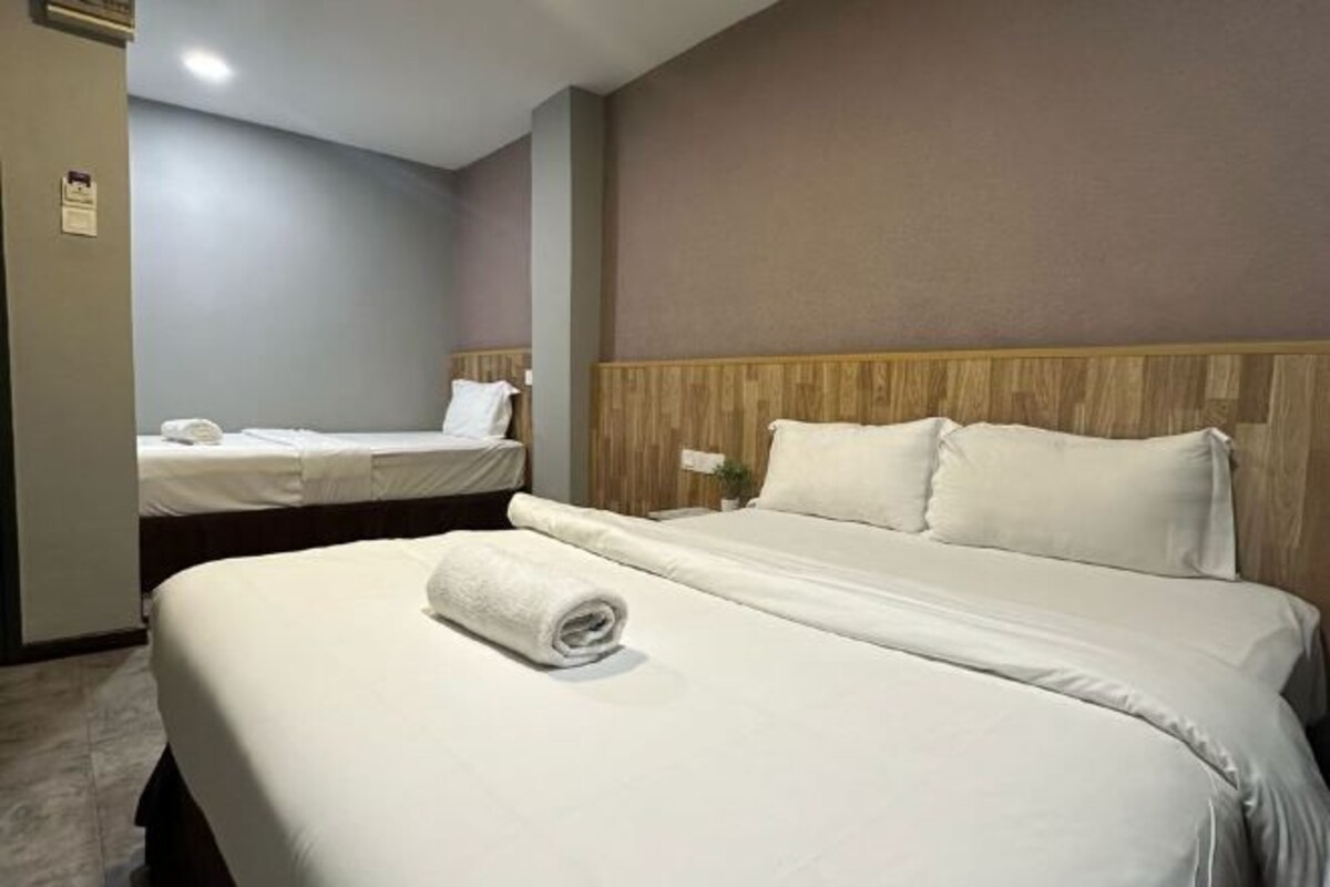 A hotel room with two beds, one larger and one smaller, both with white linens and pillows.