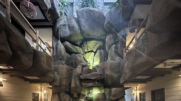 Un vestíbulo con una pared de roca, follaje artificial, una pequeña cascada y zonas de estar.