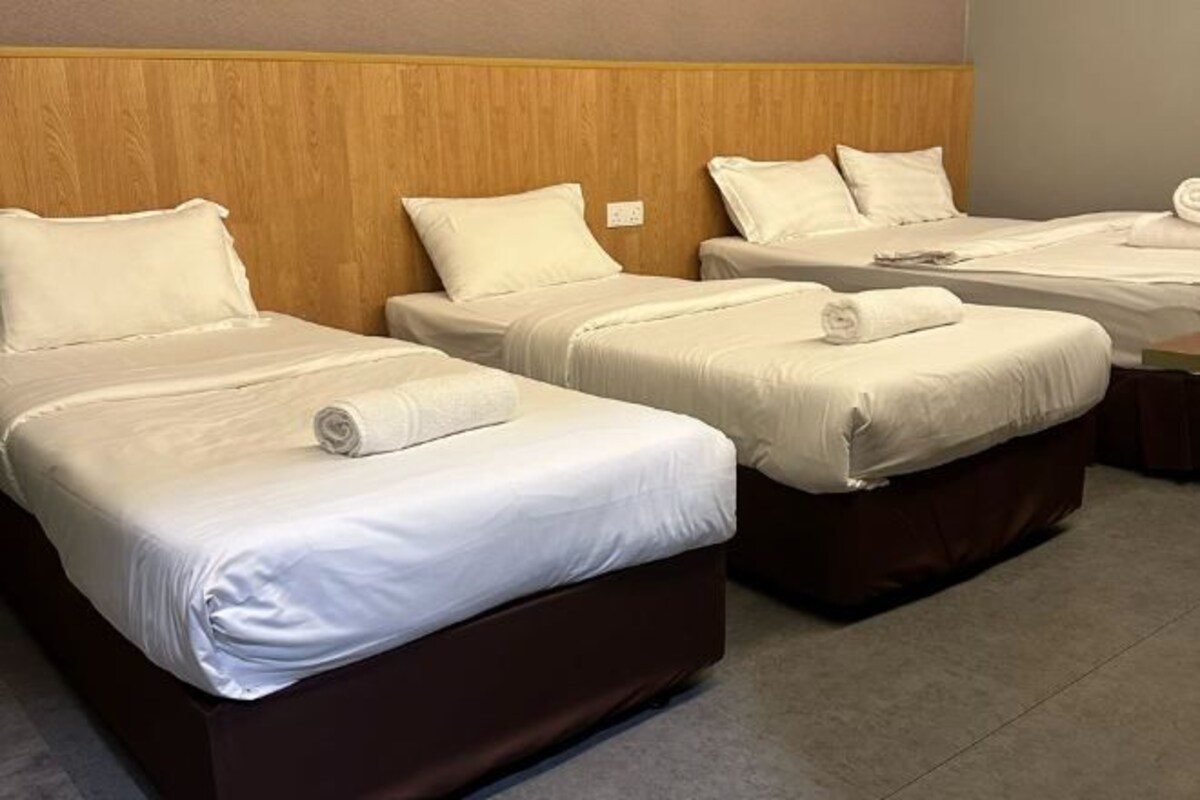A hotel room with three beds, each with white linens and pillows, a wooden headboard, and a carpeted floor.