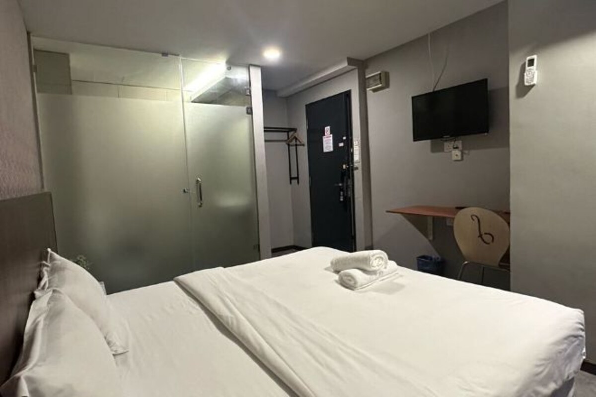 A hotel room with a bed, a TV mounted on the wall, a desk, and a wardrobe.