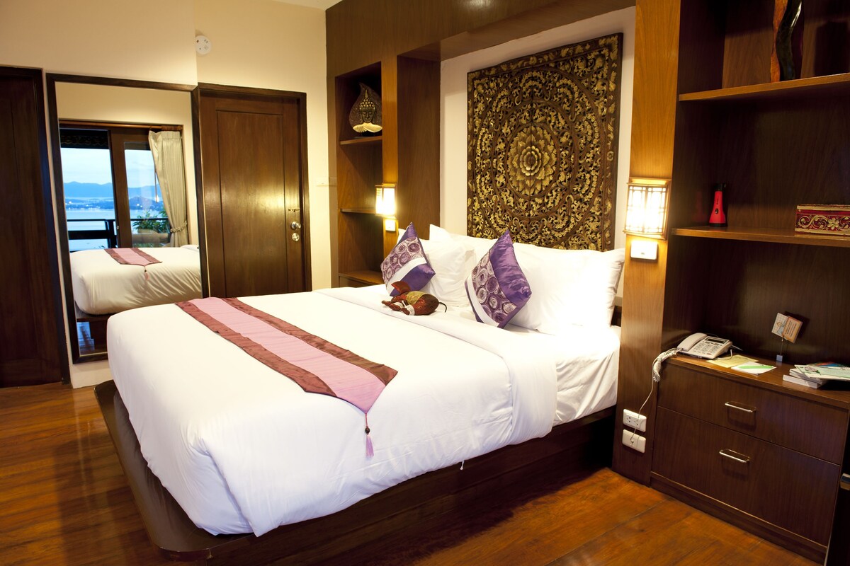 Une chambre d’hôtel avec un grand lit, une table de chevet, une lampe et une vue sur l’extérieur, visible à travers une porte.