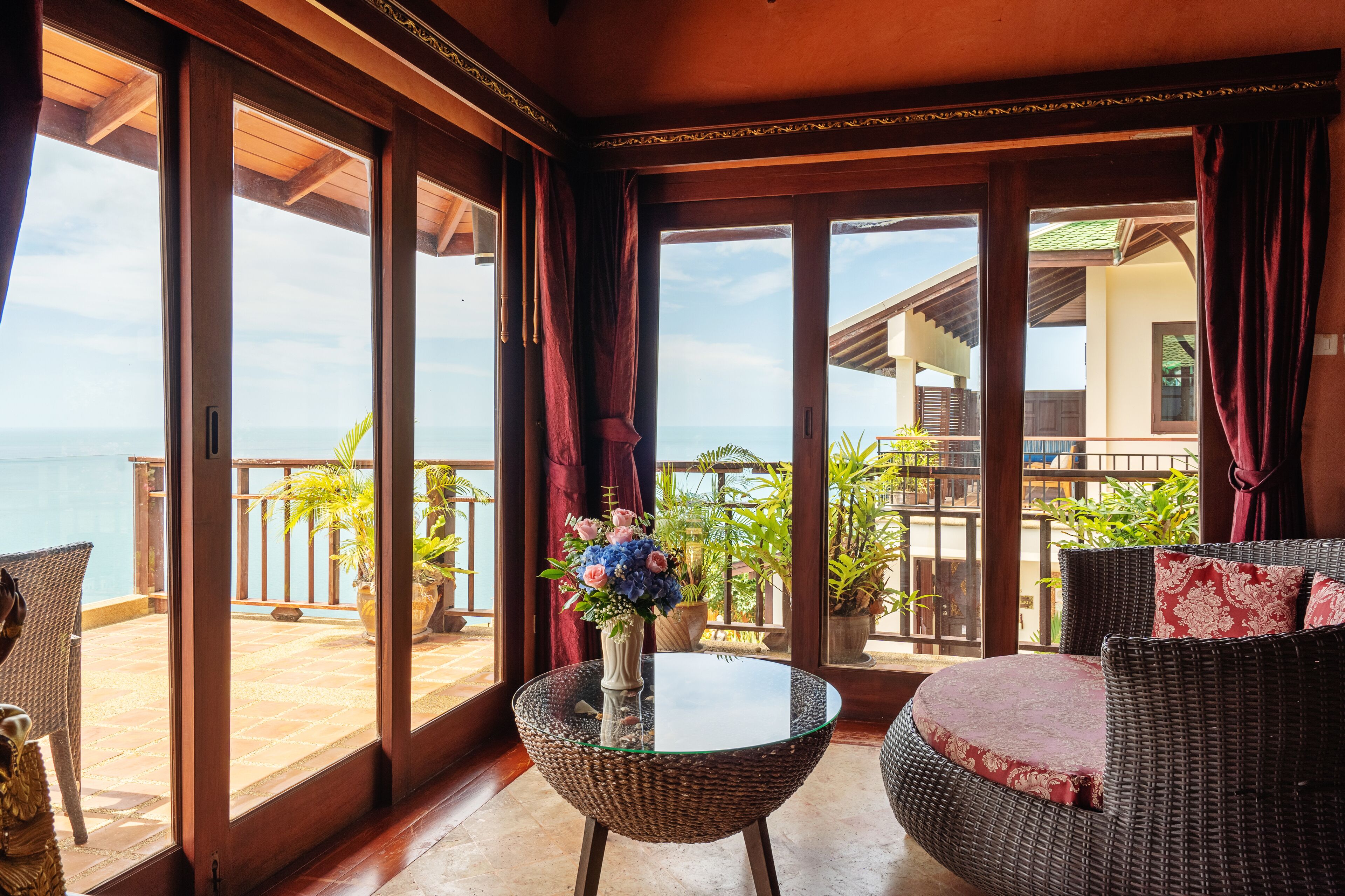 A room with a glass table, wicker furniture, and a view of the sea.