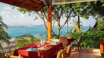 A table set for dining with a view of the ocean and hills.