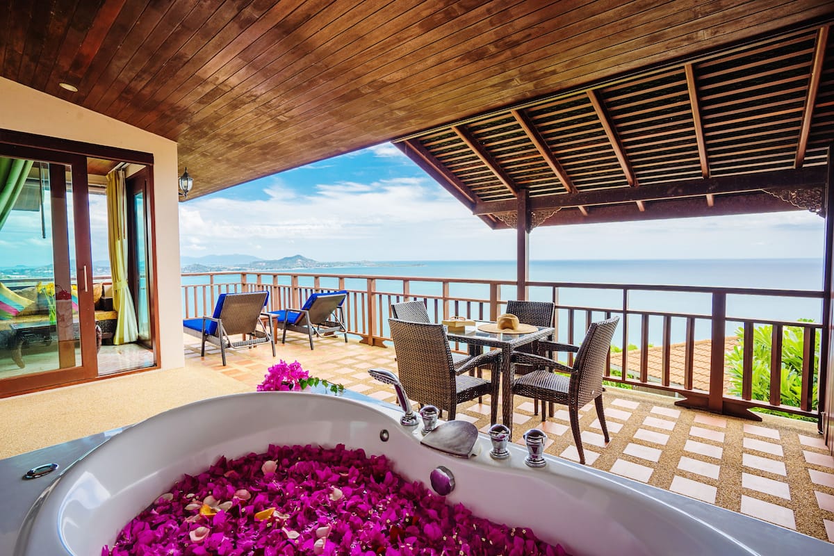 Een balkon met uitzicht op zee, een bad gevuld met rozenblaadjes en tuinmeubilair.