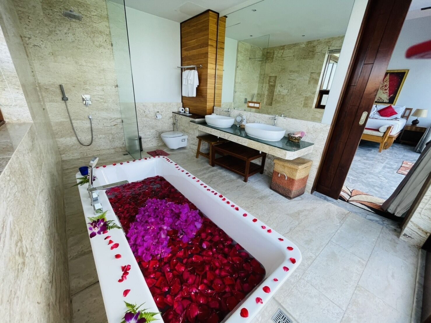 Une salle de bain moderne avec une grande baignoire remplie de pétales de roses, un meuble-lavabo à deux vasques et une douche séparée.