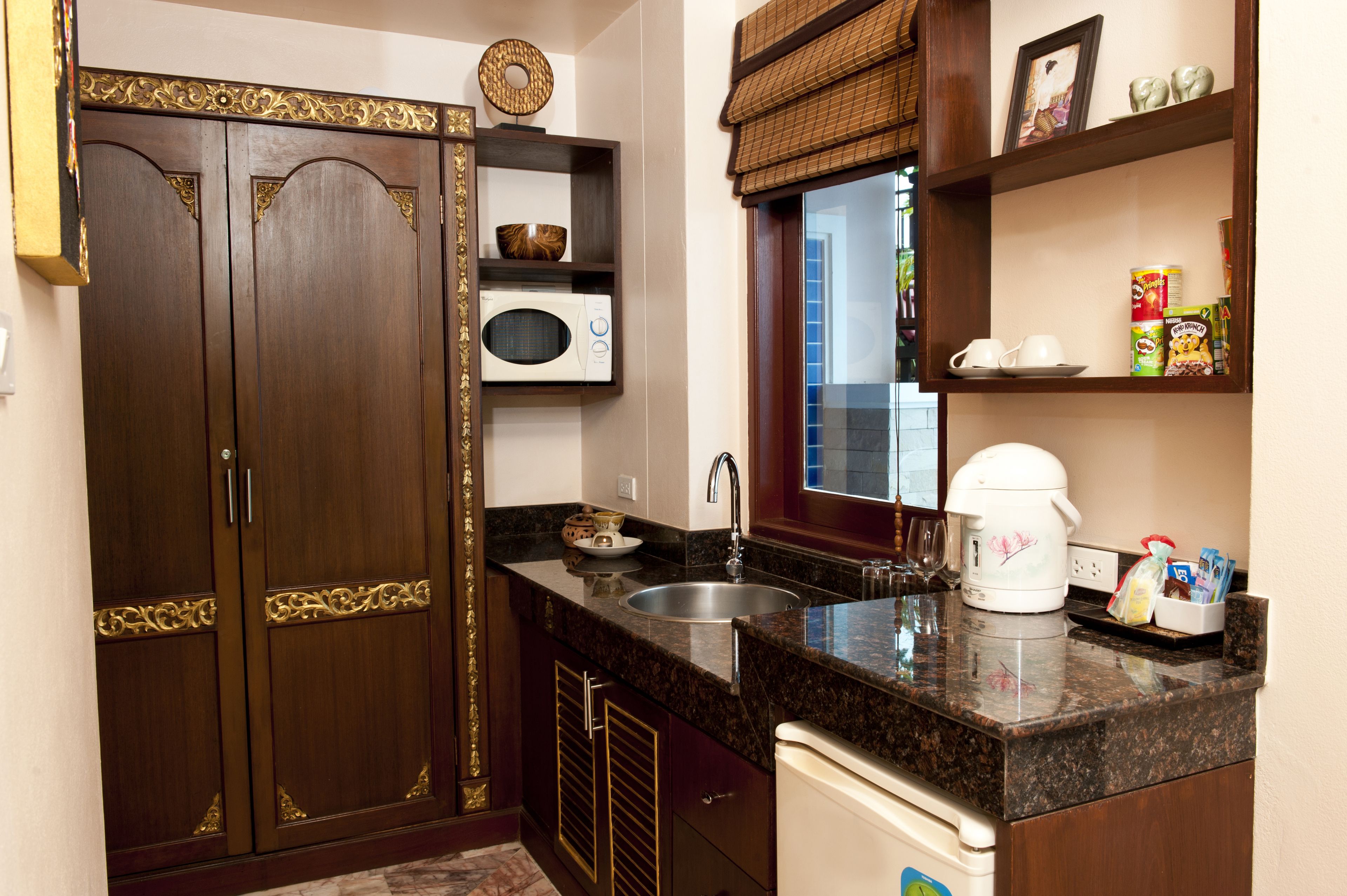 Una cocina con armarios de madera, microondas, cafetera y diversos utensilios.