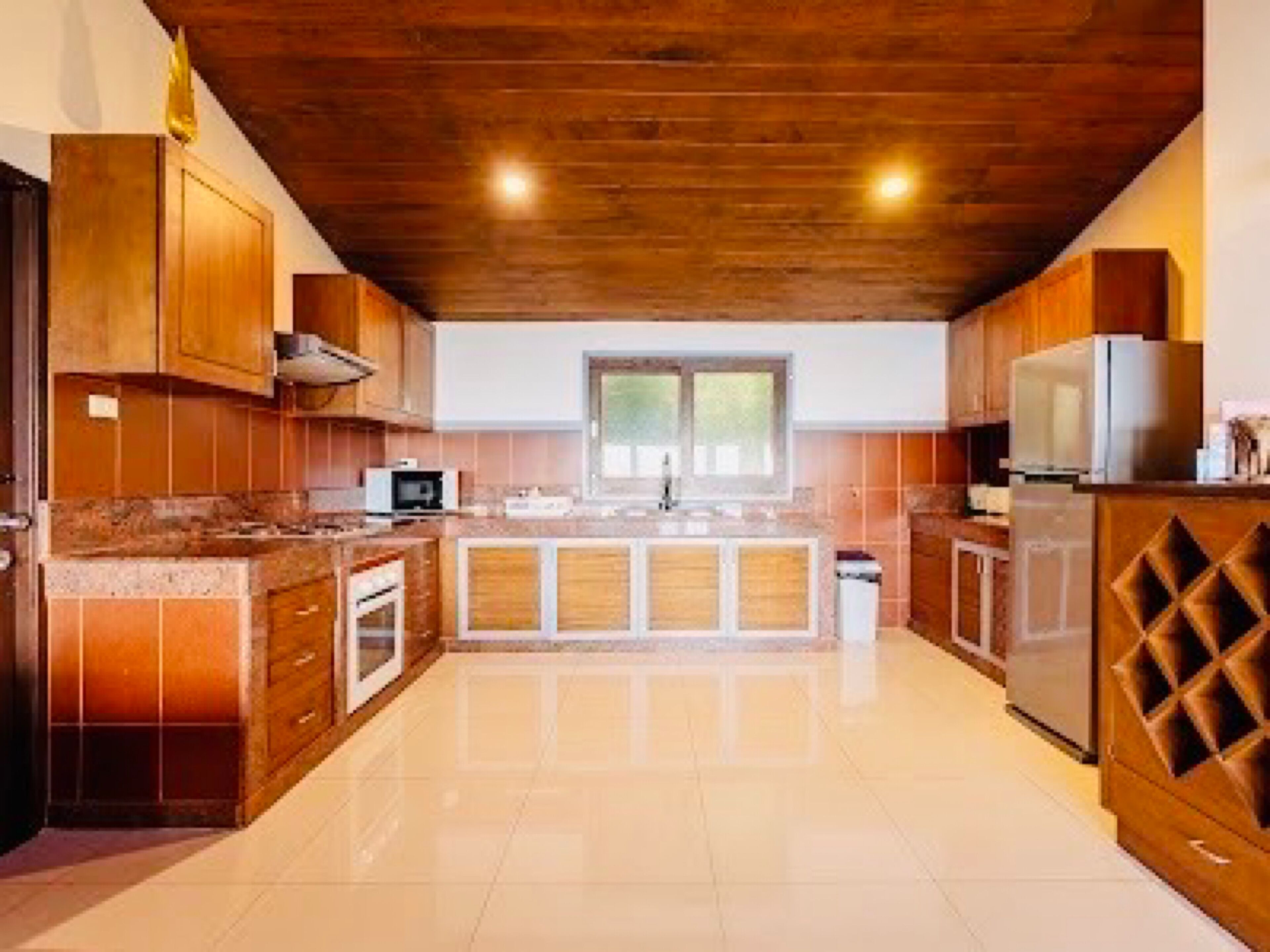 A modern kitchen with wooden cabinets, a stainless steel refrigerator, and a large window providing natural light.