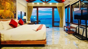 Een ruime slaapkamer met een groot bed, een plafondventilator en uitzicht op zee.