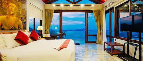 A spacious bedroom with a large bed, a ceiling fan, and a view of the sea.