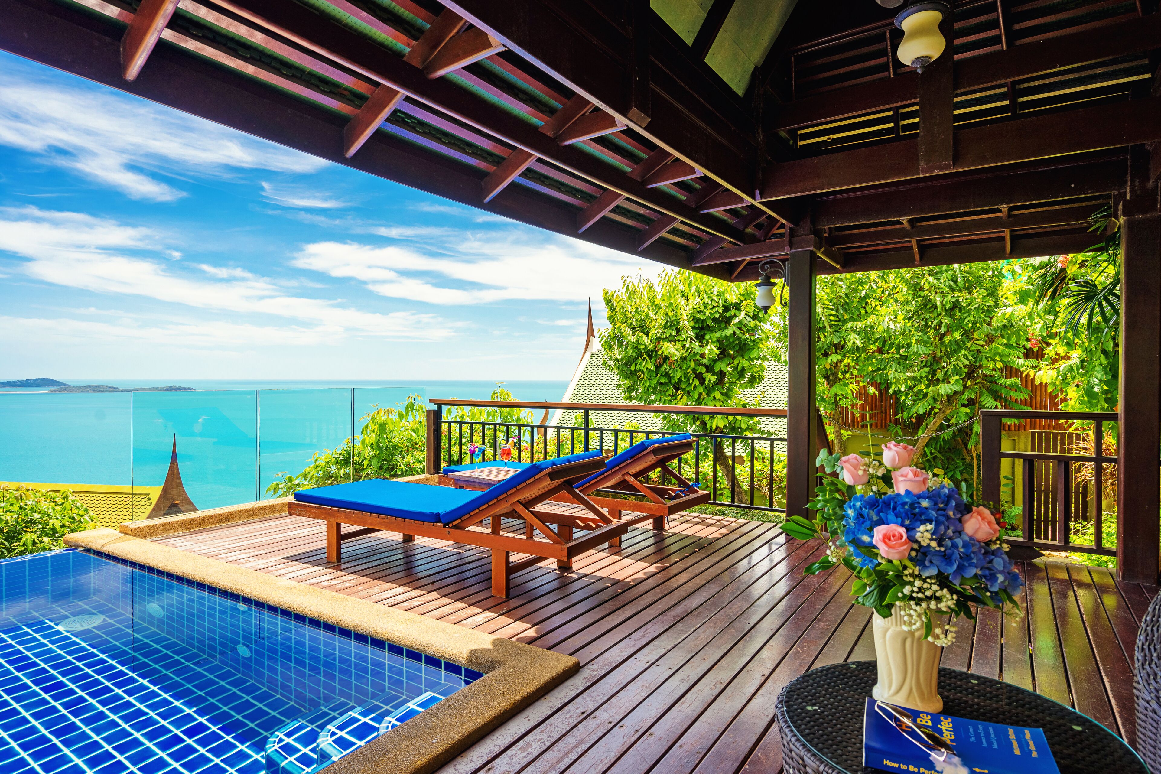 A wooden deck with a pool, lounge chairs, and a view of the sea.