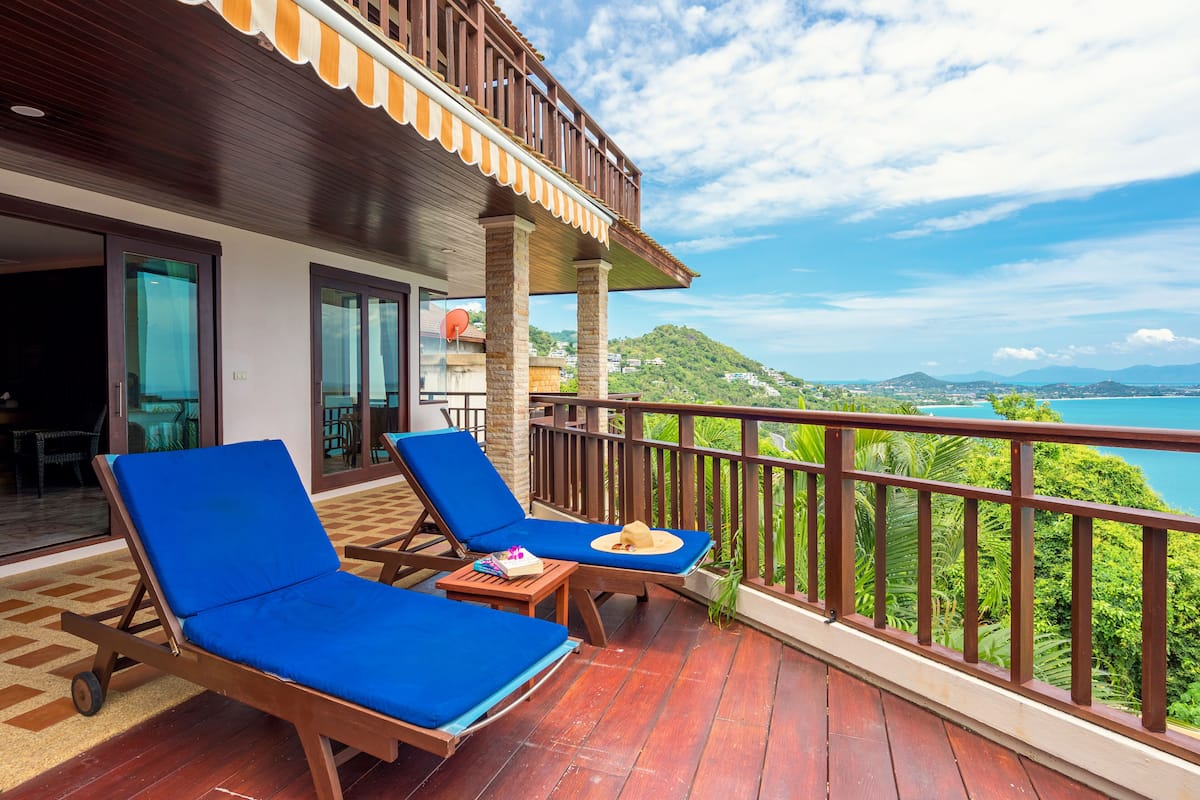 Een balkon met twee blauwe loungestoelen, een klein tafeltje en een hoed op een van de stoelen.