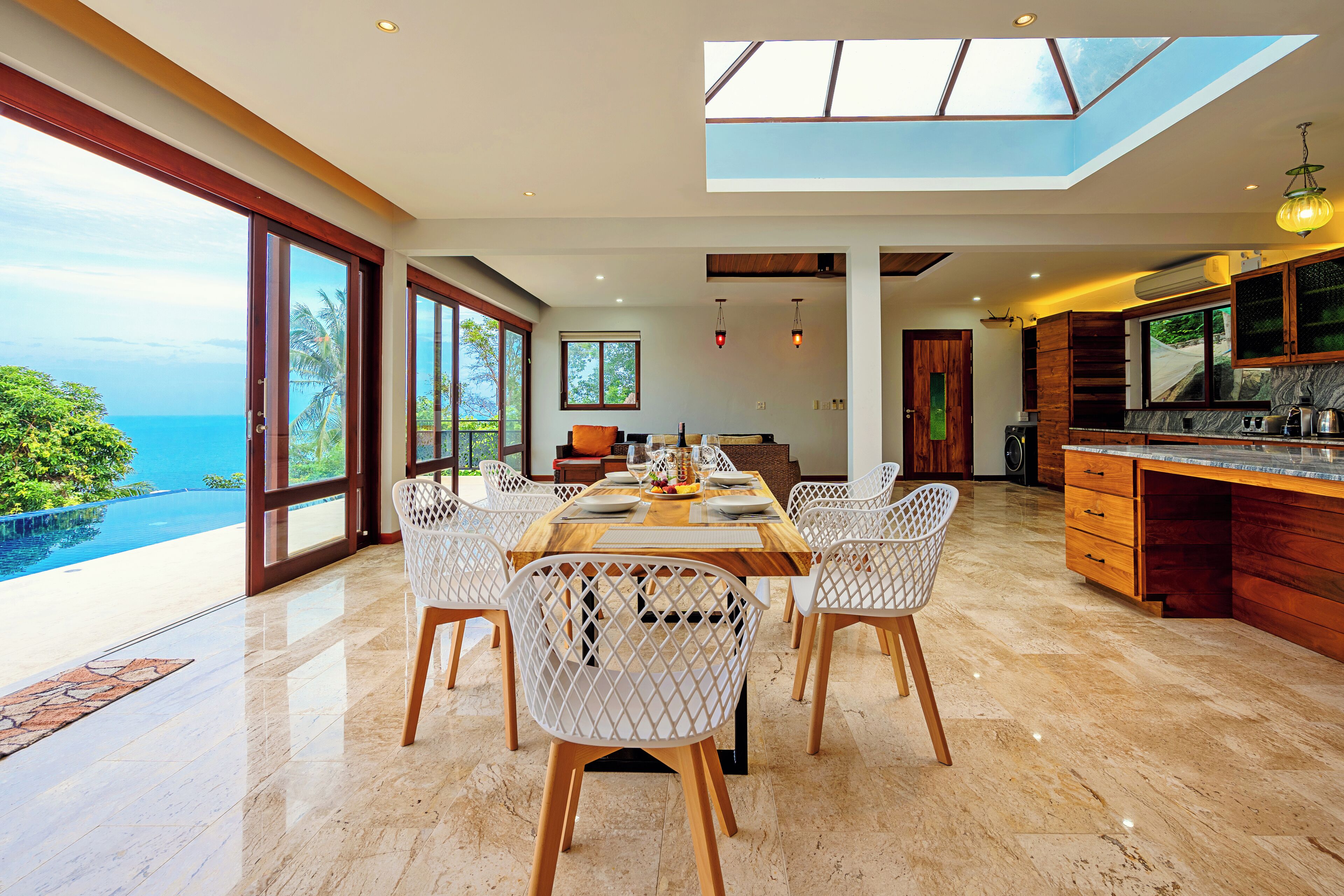 A modern dining area with a large table, white chairs, and a view of the ocean.