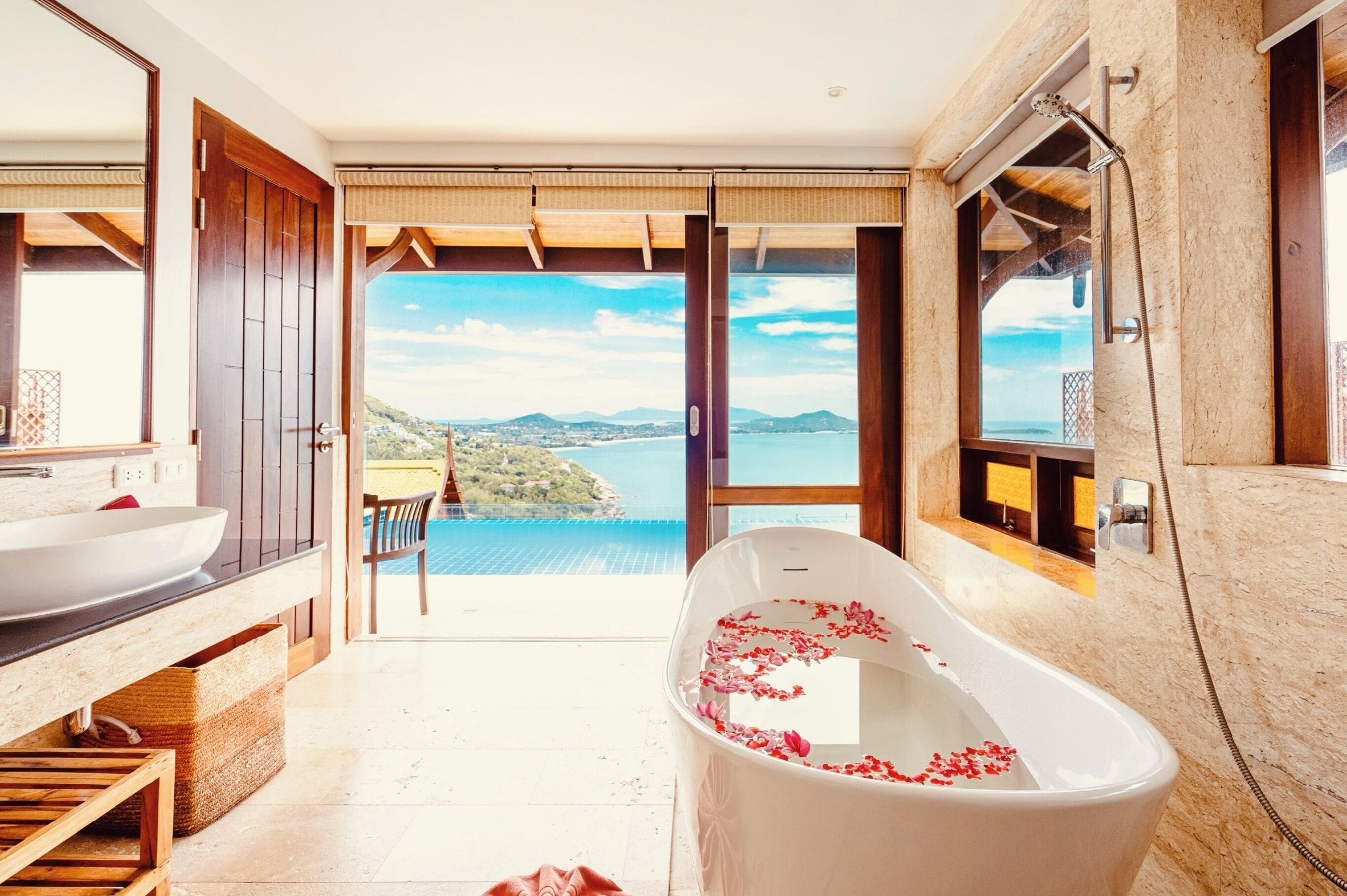 A modern bathroom with a freestanding bathtub, a large mirror, and a view of a coastal landscape.