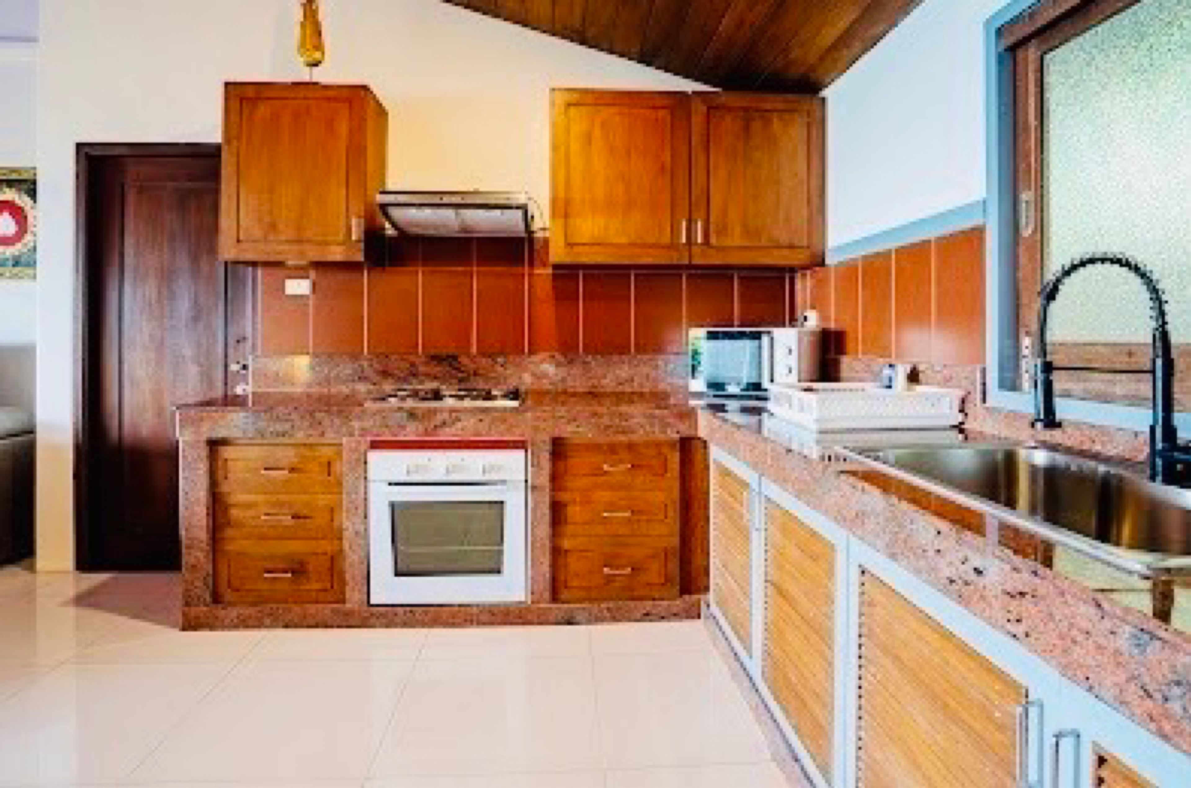 A kitchen with wooden cabinets, a built-in oven, a microwave, and a stainless steel sink.