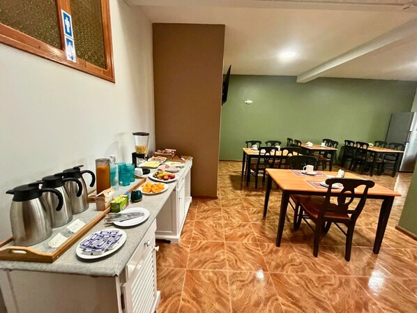 A dining area with multiple tables and chairs, a buffet counter with food items, and a coffee station with kettles and cups.