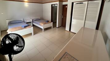 Ein kleines Zimmer mit Bett, einem Tischchen, einem Ventilator und einem Kleiderschrank.