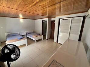 A compact room with a bed, a small table, a fan, and a wardrobe.