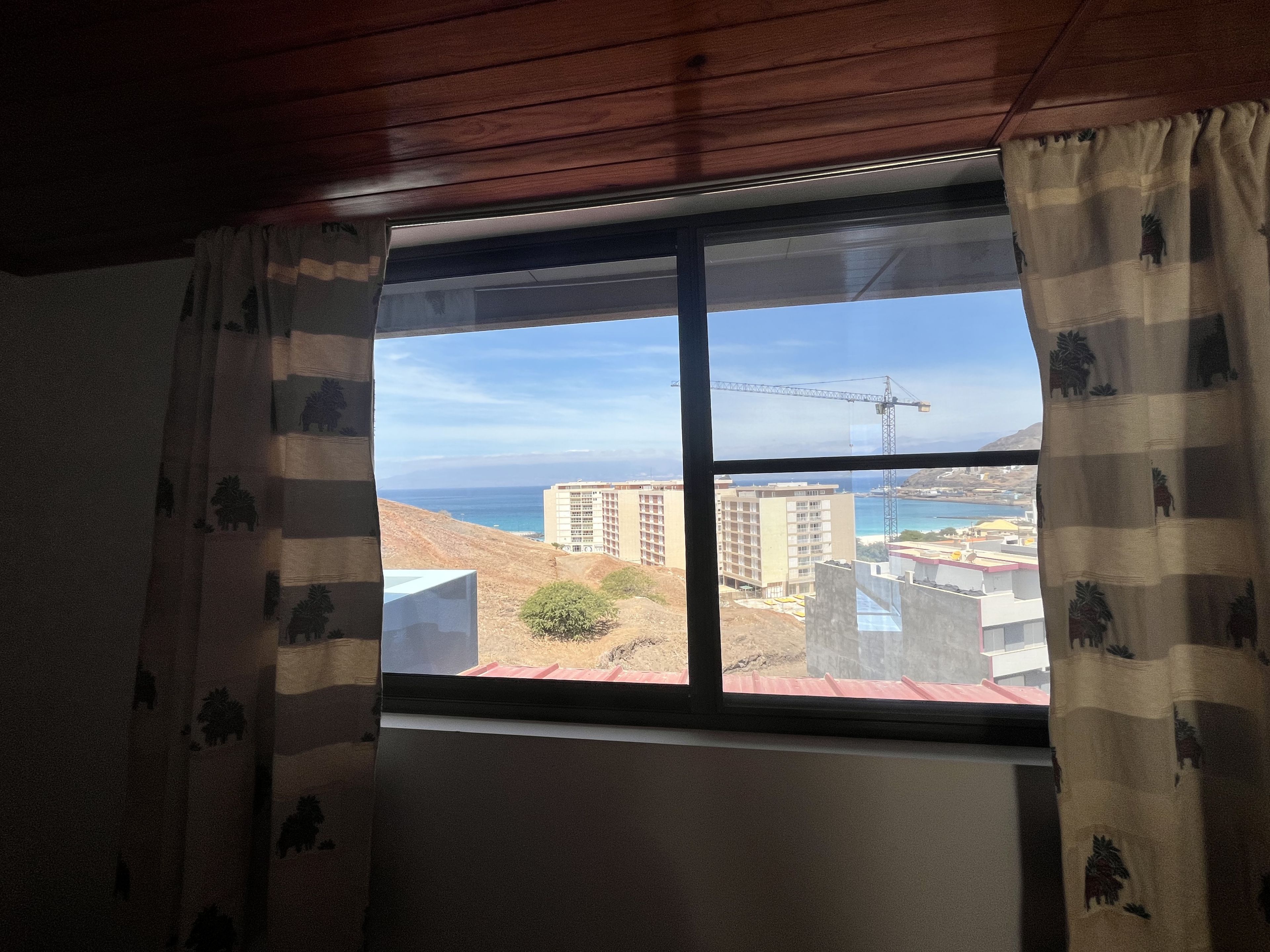 Ein Fenster mit Blick auf eine Küstenstadtlandschaft, darunter Gebäude und ein Kran.