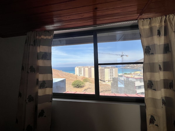 A window with a view of a coastal cityscape, including buildings and a crane.