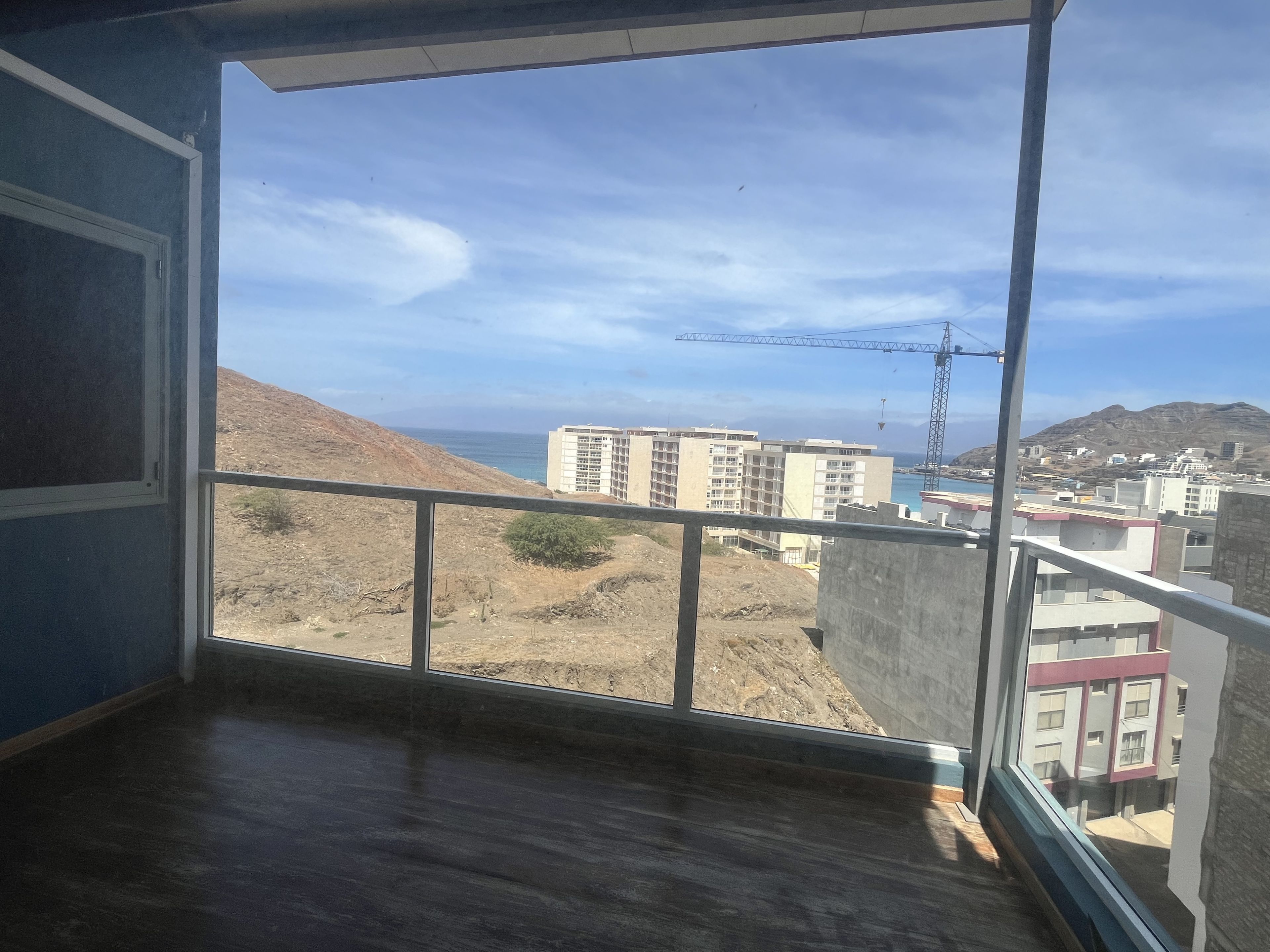 Una habitación con un ventanal grande que da a una obra en construcción, edificios y un paisaje montañoso.