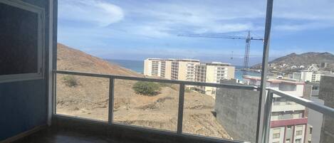 Una habitación con un ventanal grande que da a una obra en construcción, edificios y un paisaje montañoso.