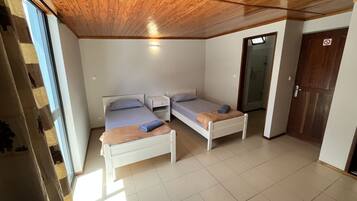 Quarto com duas camas de solteiro, teto de madeira, porta branca e uma janela.