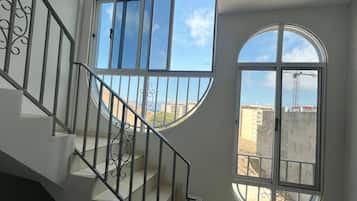 Una escalera con barandilla metálica que lleva a una plataforma con ventanas amplias que ofrecen vistas de edificios y una grúa.