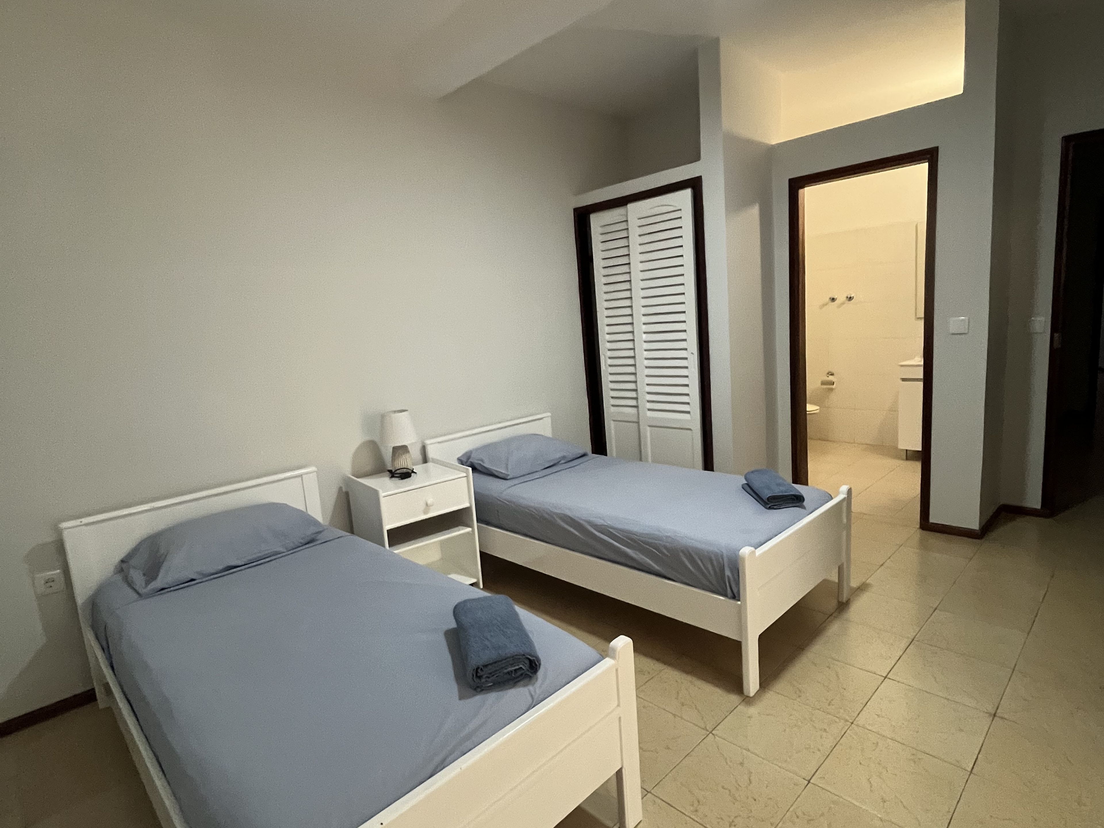 Een slaapkamer met twee eenpersoonsbedden, een nachtkastje met een lamp en een deur naar een badkamer.