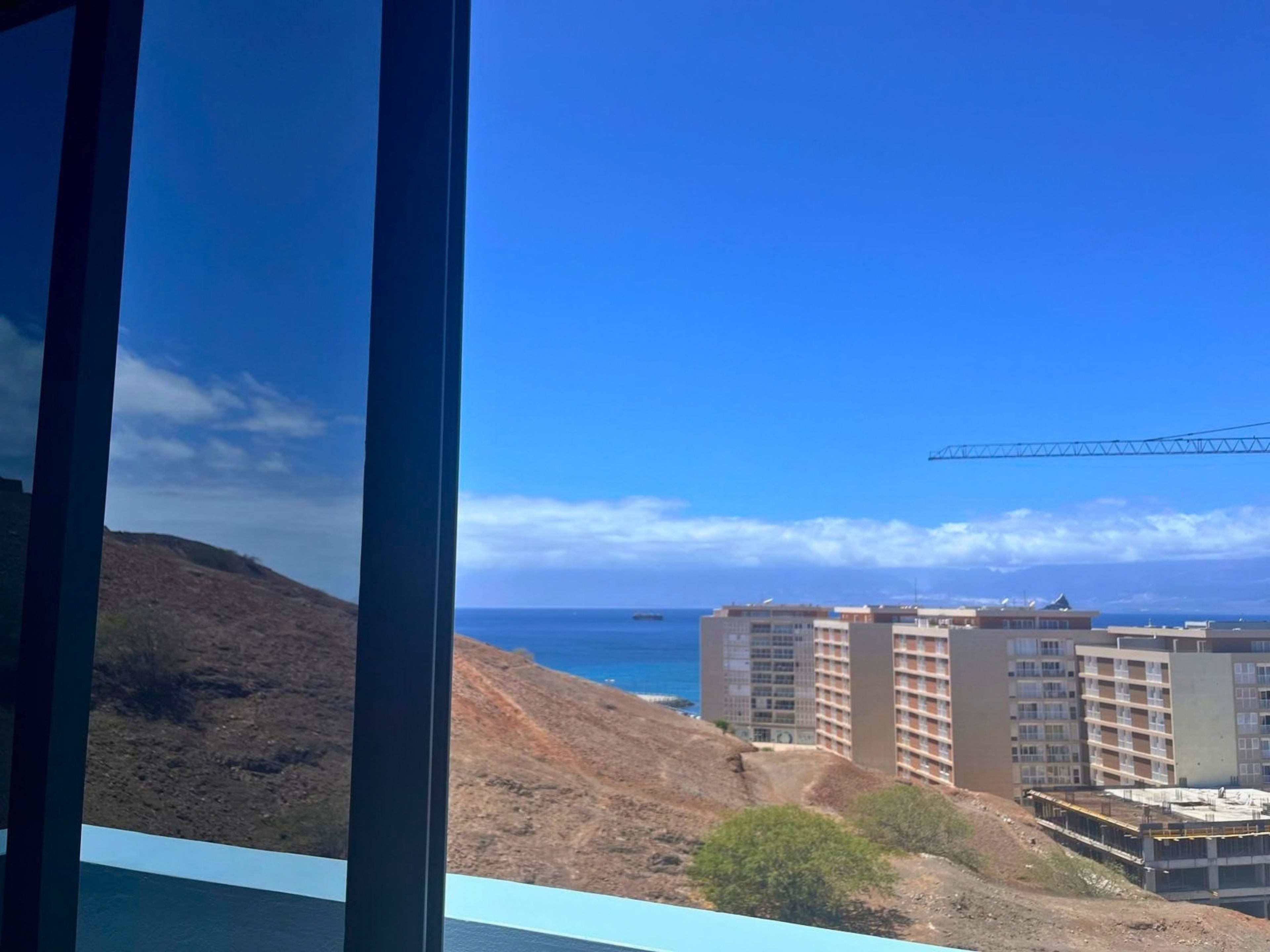 A coastal view with a construction site, buildings, and a crane.