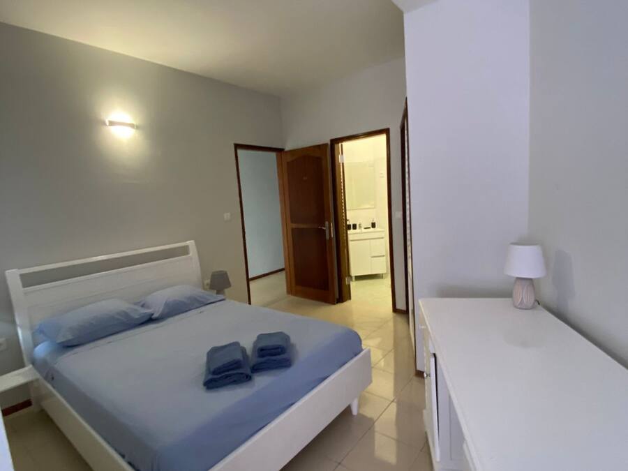 Un dormitorio con cama, mesita de noche, lámpara y una puerta que da al baño.