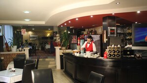 A restaurant with a bar area, tables, chairs, and a television screen. - Hotel Adria (Pristina)