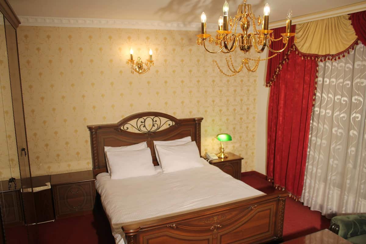 Una cama bien hecha con cabecera de madera, una mesita de noche con lámpara y un candelabro arriba.