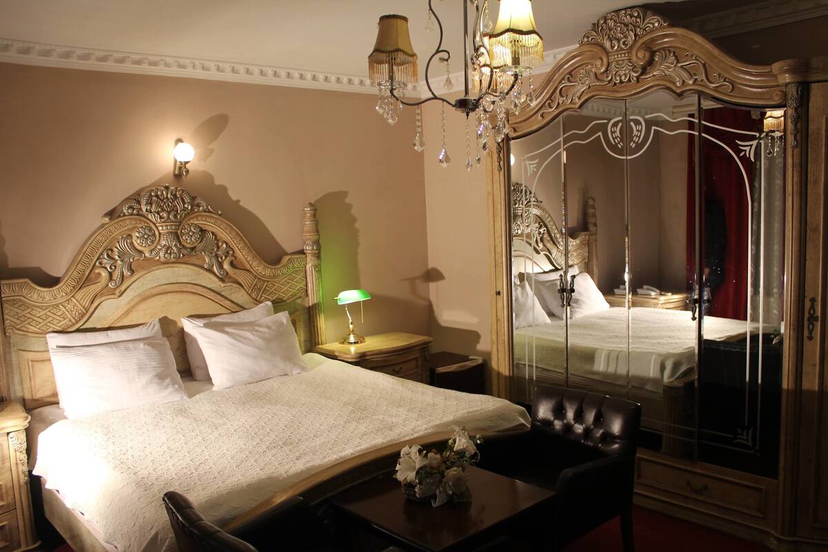 Habitación de hotel con una cama grande, una mesita de noche, una lámpara, un espejo y un sillón de cuero negro.