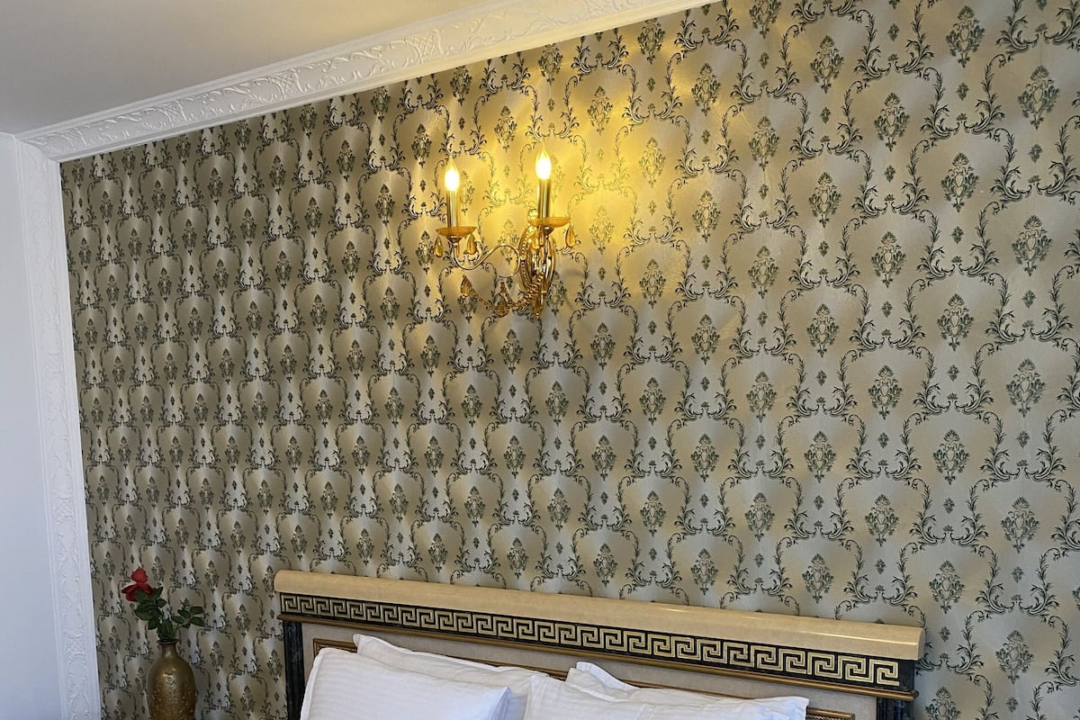 Habitación de hotel con cama, mesita de noche y teléfono, y una pared con papel tapiz estampado.