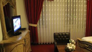 A hotel room with a television on a wooden cabinet, a leather chair, a wooden table with a vase of flowers, and a bed with a white comforter.