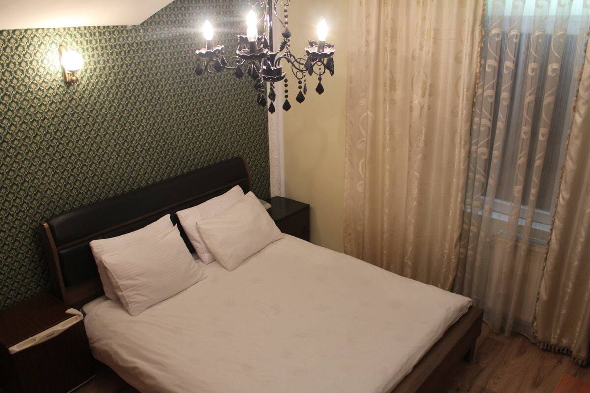Una cama bien hecha con cabecera de madera, una mesita de noche con lámpara y un papel tapiz estampado.