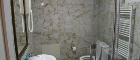 A bathroom with a marble floor, a sink, a toilet, and a glass shower enclosure.