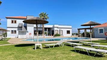 A modern building with a swimming pool, outdoor seating, and palm trees.