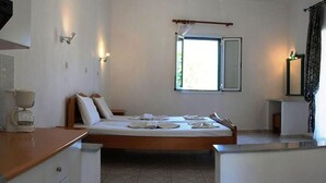 A bedroom with a bed, bedside tables, a window, and a kitchenette area. - Zeus Hotel (Samos)