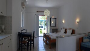 A bedroom with a bed, a desk, and a chair. There is a balcony with a view of palm trees. - Zeus Hotel (Samos)
